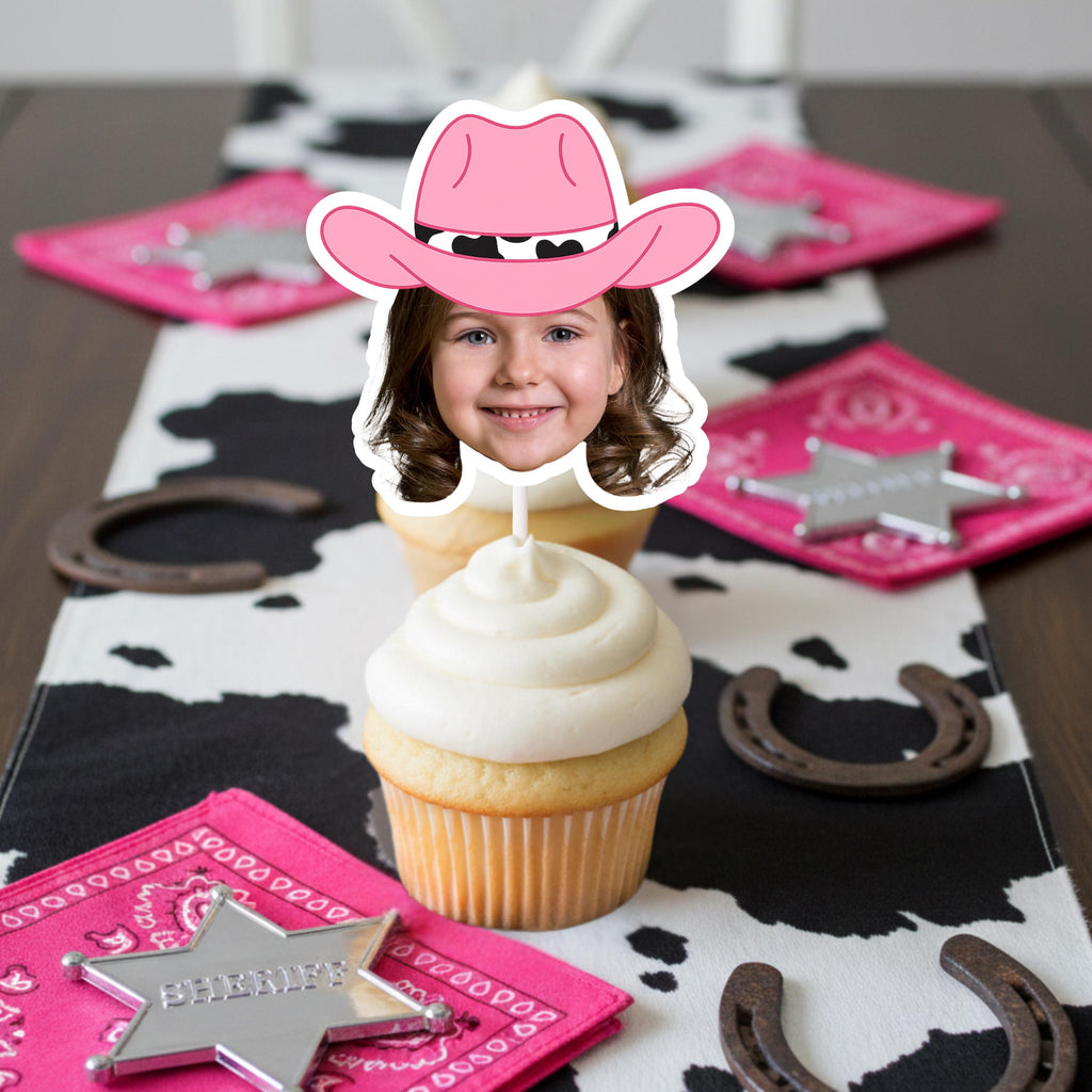Cupcake with a pink cowboy hat on top, placed on a table with cowgirl-themed decorations.