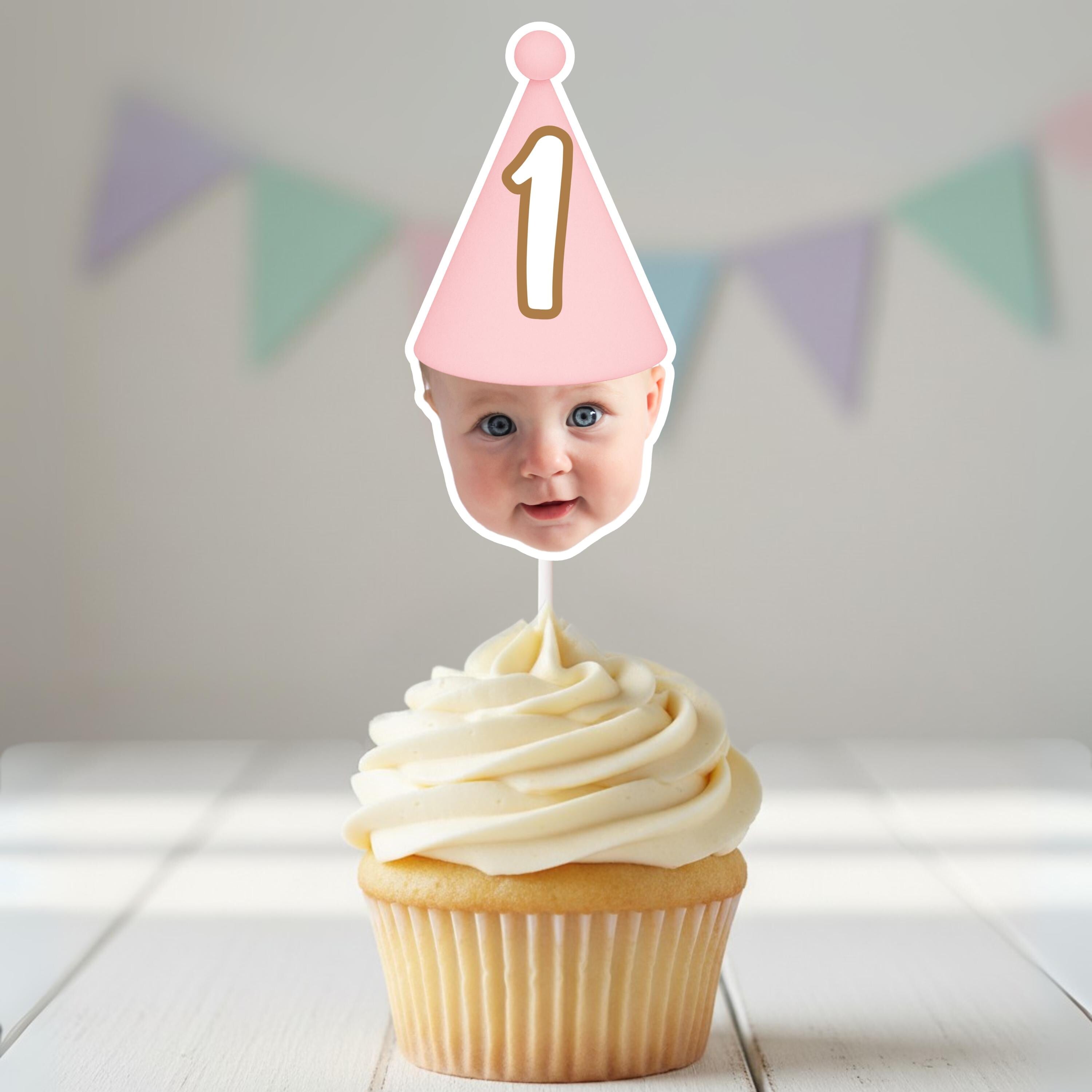 Cupcake with a baby's face on a topper with a pink party hat and number '1'.