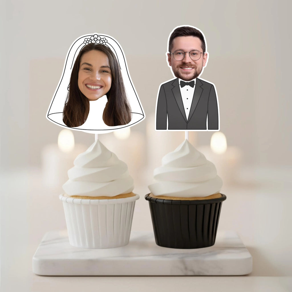 Two cupcake toppers with cut-out faces of a bride and groom on a marble base.