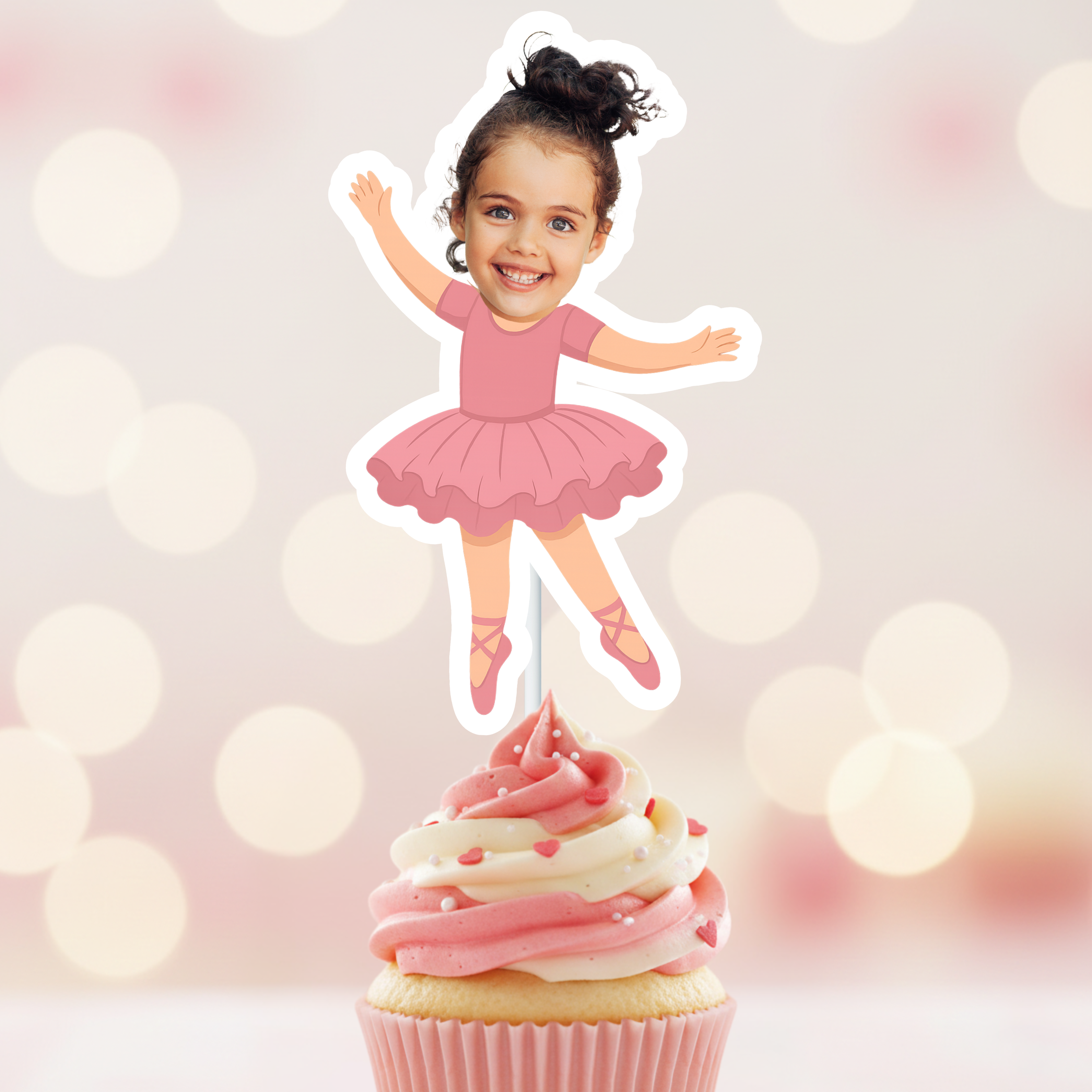 Cake topper of a girl in a pink ballet outfit on a cupcake with a blurred light background