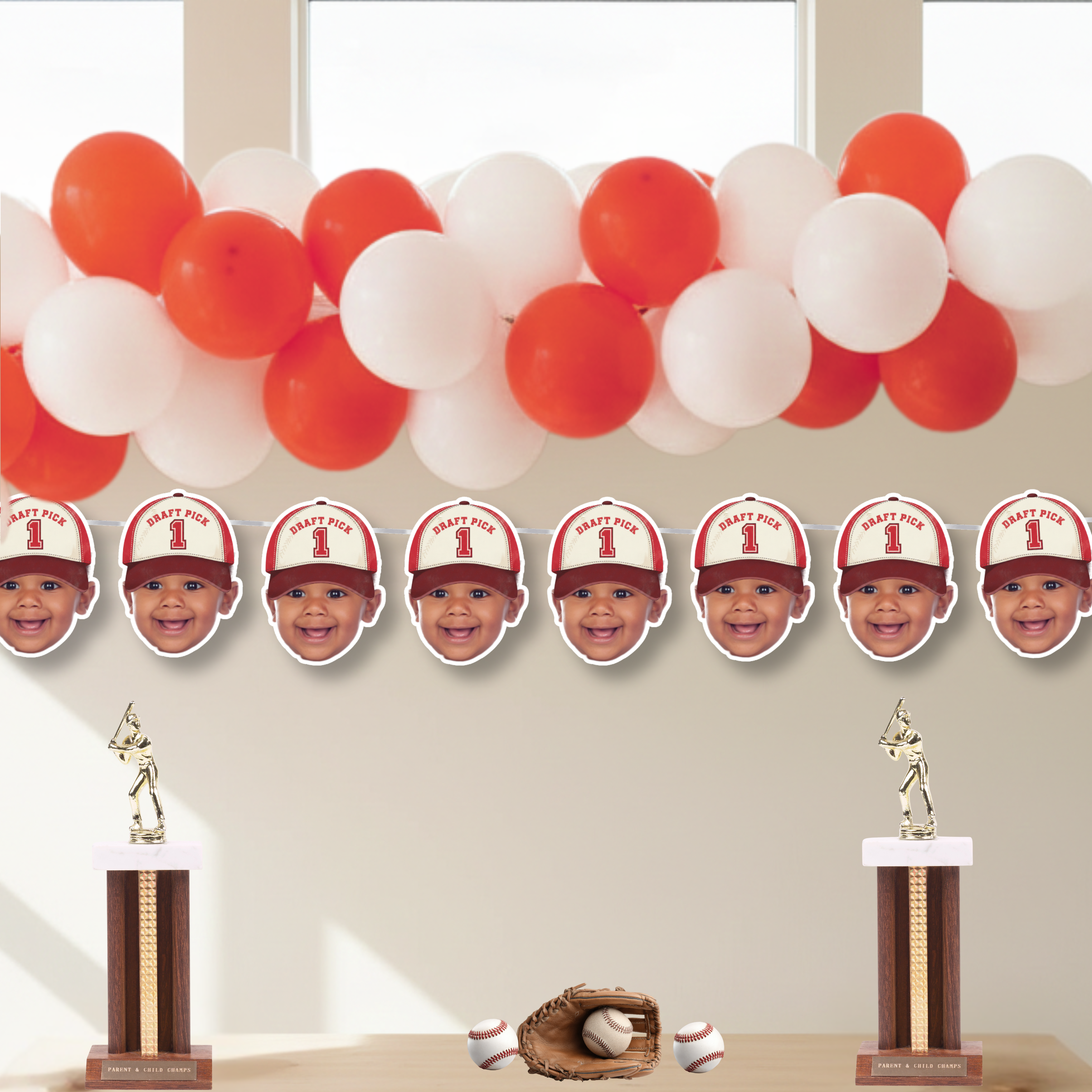 Custom baseball first birthday banner with baby photo wearing Draft Pick 1 hat, styled with red and white balloon garland, baseball trophies, glove and balls for Rookie of the Year sports themed birthday party decor.