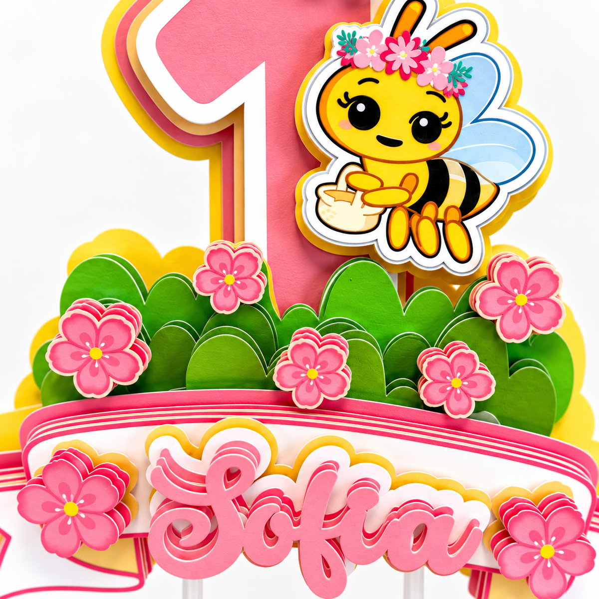 Close up of personalized bee cake topper with layered cardstock flowers green grass pink number one and dimensional Sofia name