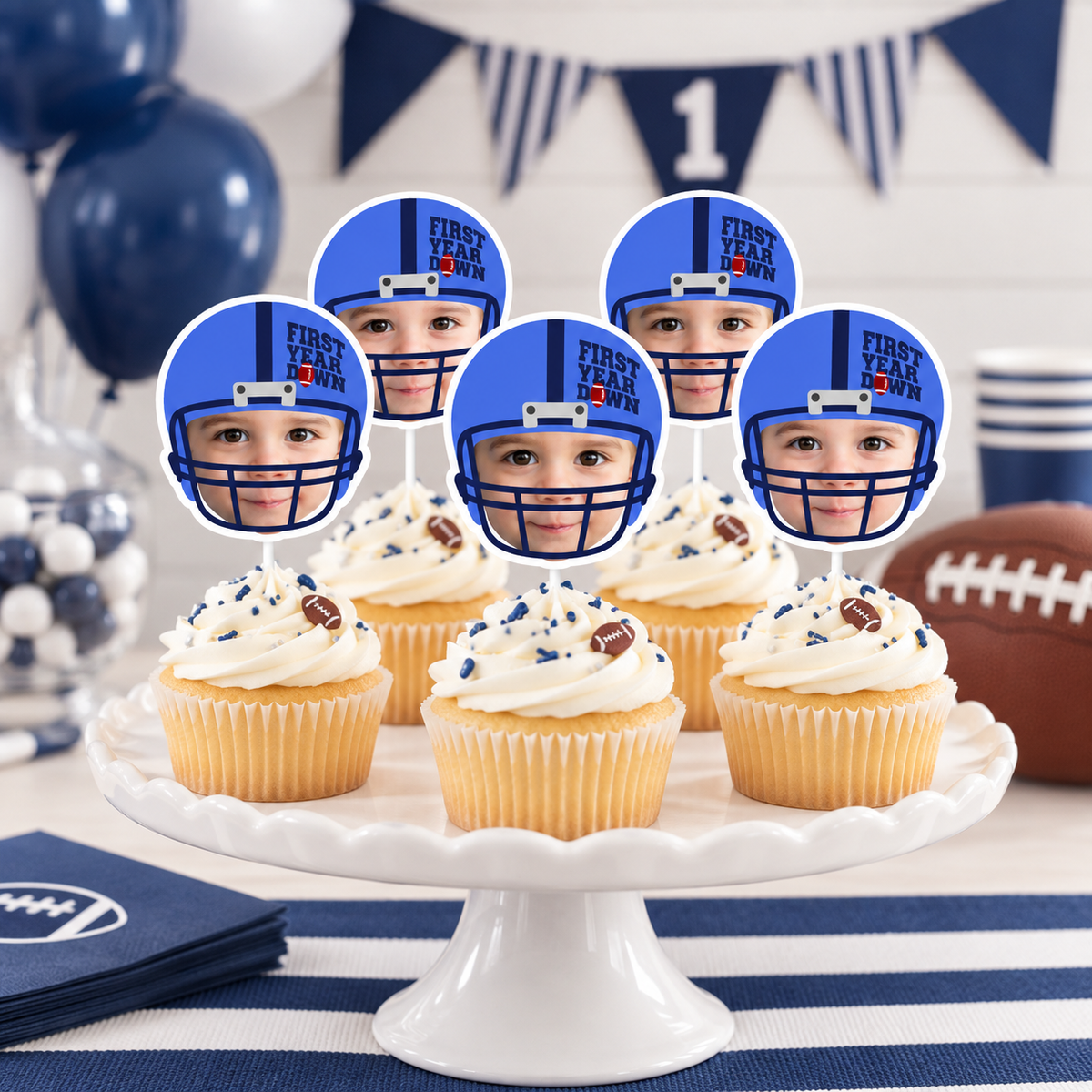 Personalized First Year Down football photo cupcake toppers with child faces in blue football helmets displayed on cupcakes for a football first birthday celebration
