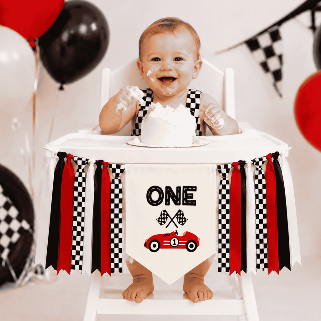 Baby celebrating a first birthday cake smash with a personalized Fast One highchair banner featuring a race car design, checkered ribbons, and red racing decor for a Formula WON birthday party.