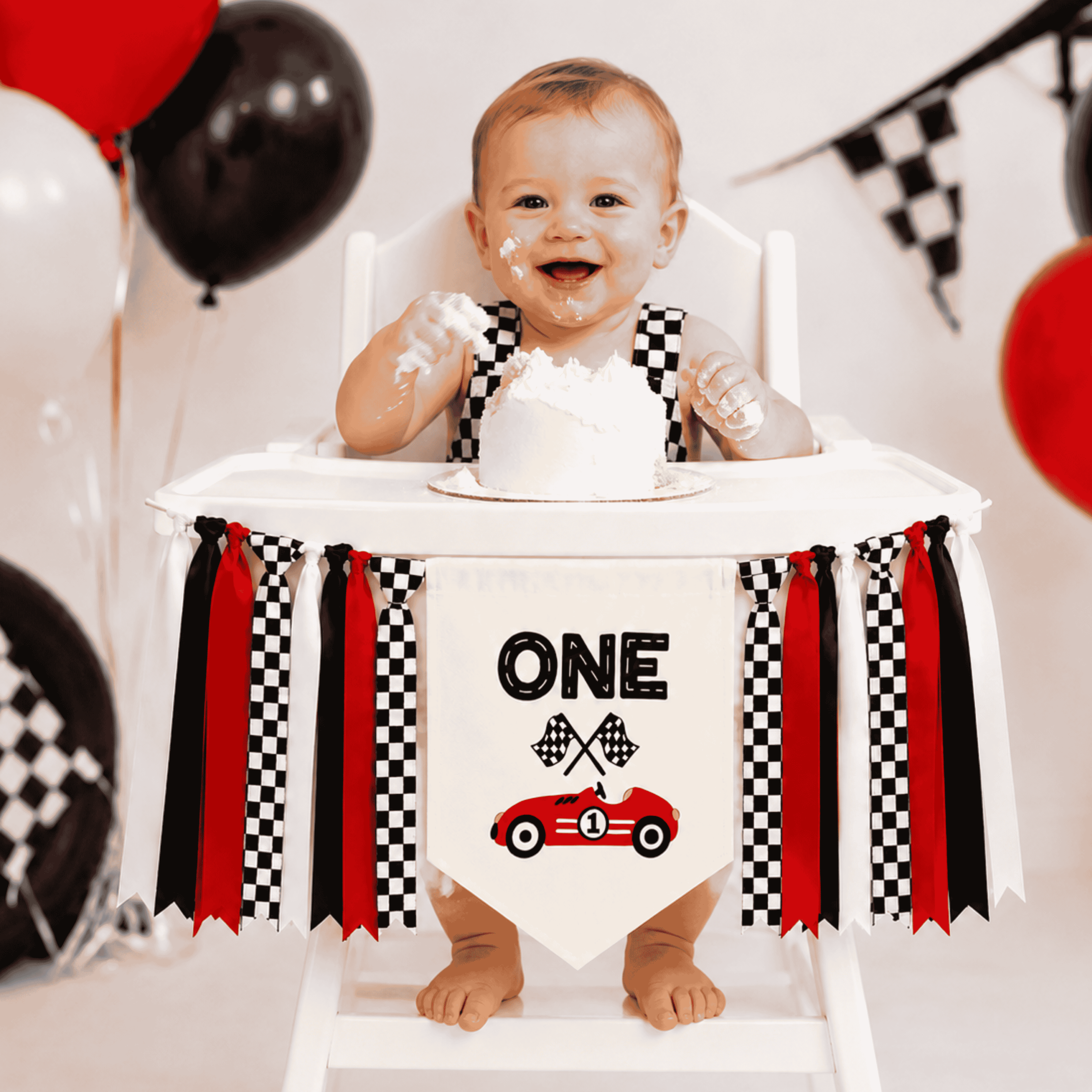 Baby celebrating a first birthday cake smash with a personalized Fast One highchair banner featuring a race car design, checkered ribbons, and red racing decor for a Formula WON birthday party.