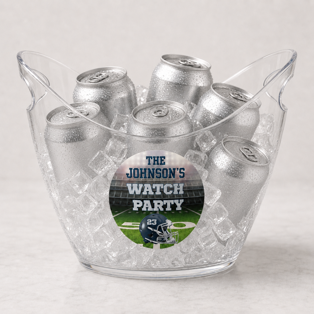 A clear plastic beverage bucket filled with ice and multiple silver aluminum cans, featuring a custom circular sticker that reads 'THE JOHNSON'S WATCH PARTY' with a football field and helmet graphic.