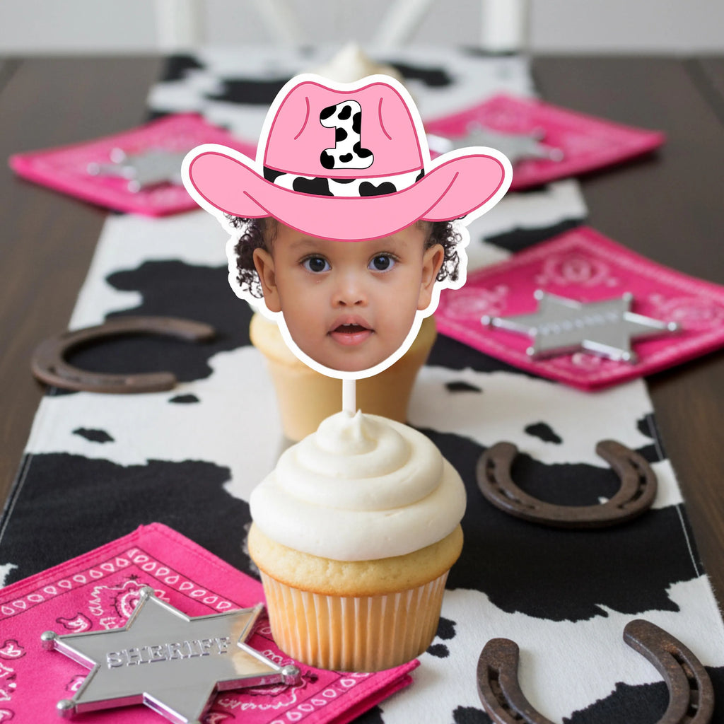 Cupcake with a pink cowboy hat decoration on a table with cowgirl-themed decor.