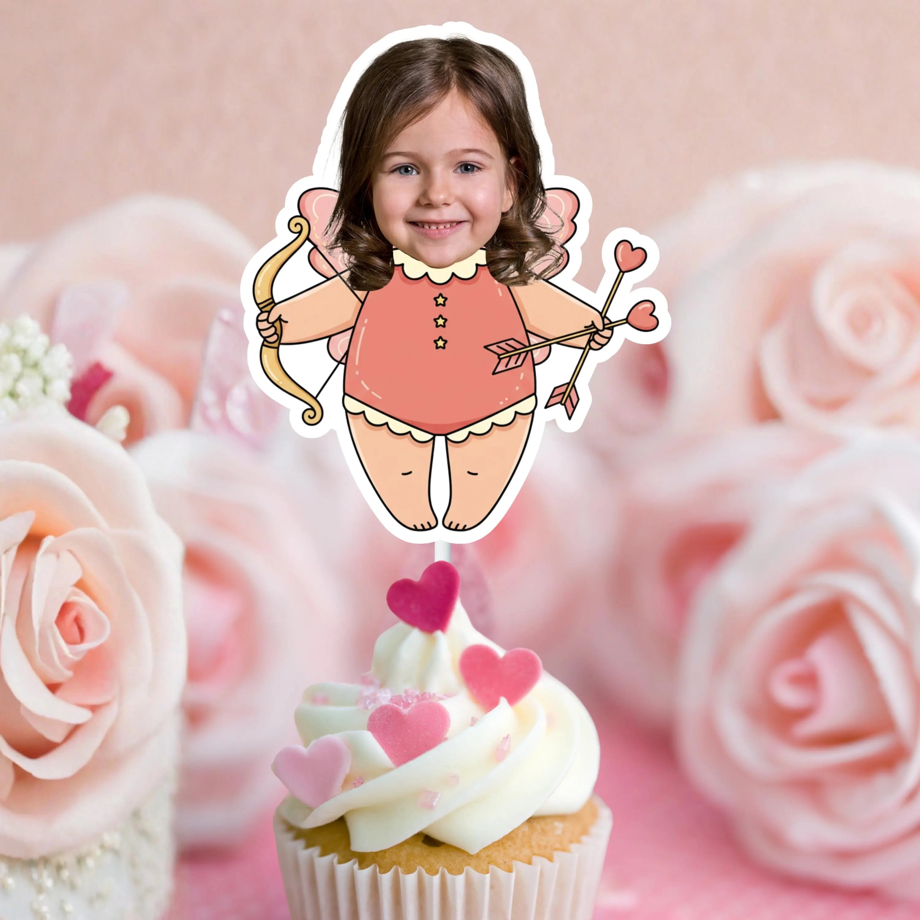 Cupcake with pink heart decorations and a sticker of a girl with fairy wings and a bow on a pink floral background.