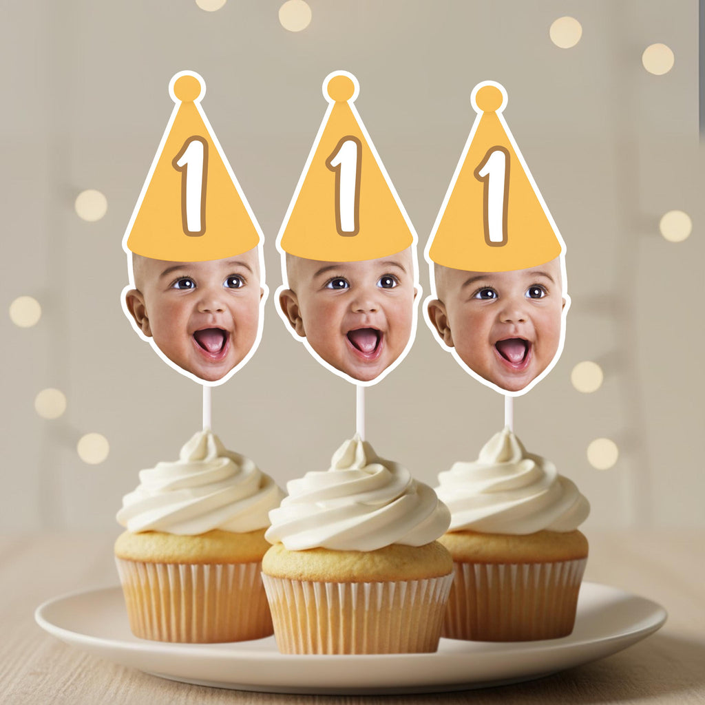 Three cupcakes with cream and yellow cake toppers featuring baby faces on a neutral background.