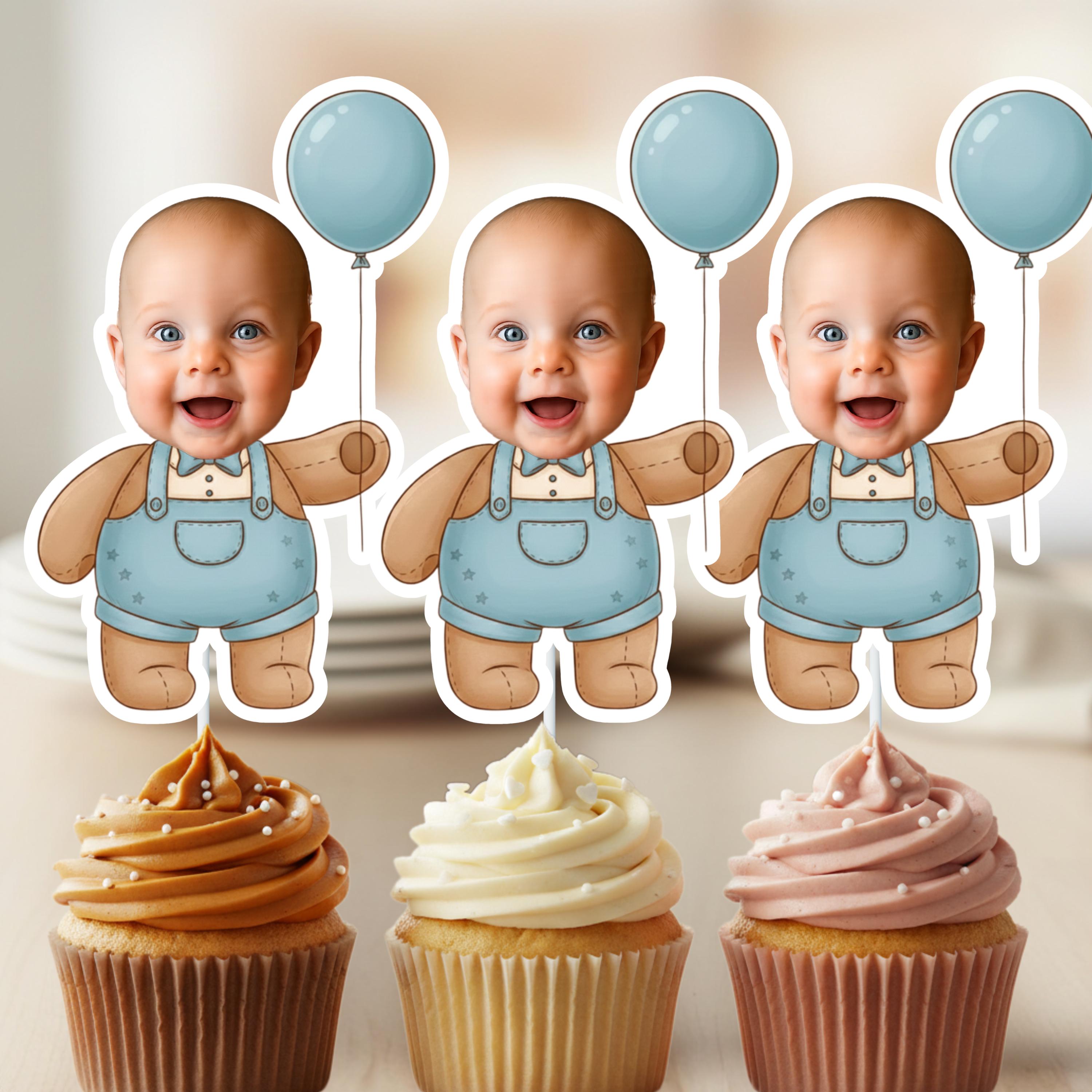 Three identical baby figurines in blue overalls with balloons above, standing next to three frosted cupcakes.
