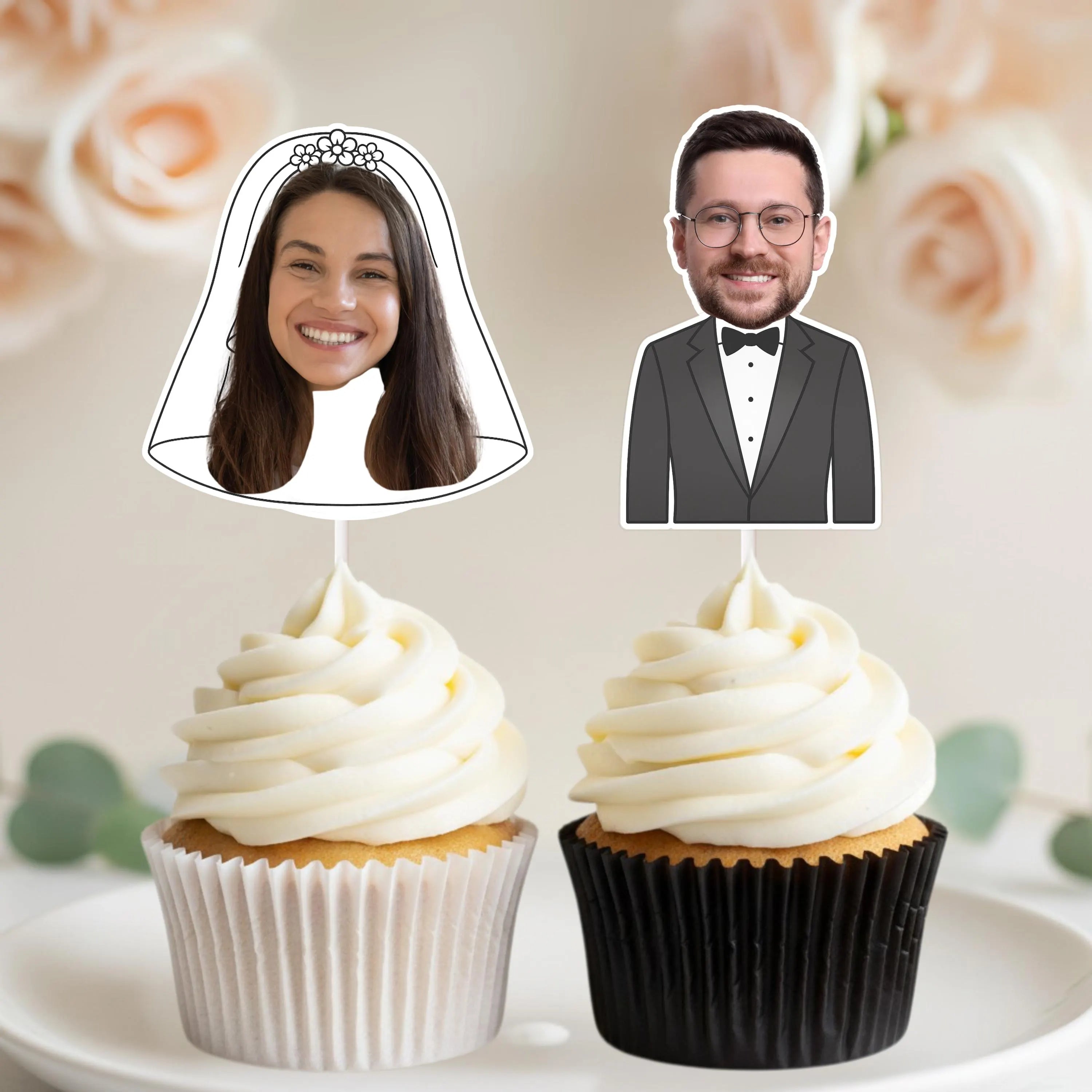 Two cupcakes with face cutouts of a bride and groom on a floral background