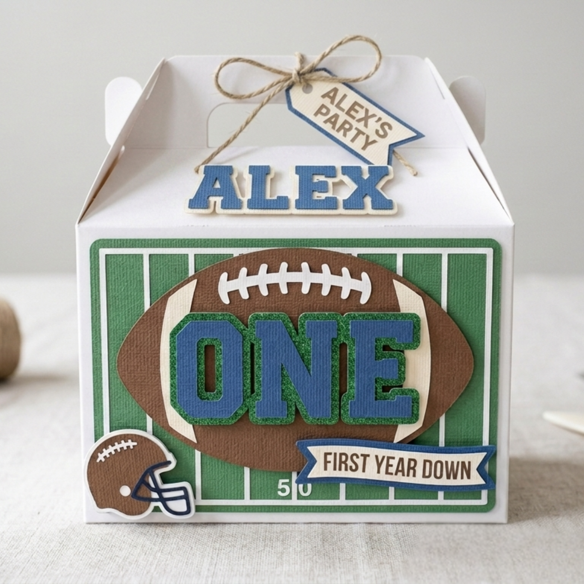 Custom football themed First Year Down birthday party favor box featuring layered cardstock football field design, raised number one centerpiece, and handmade first birthday party decorations.