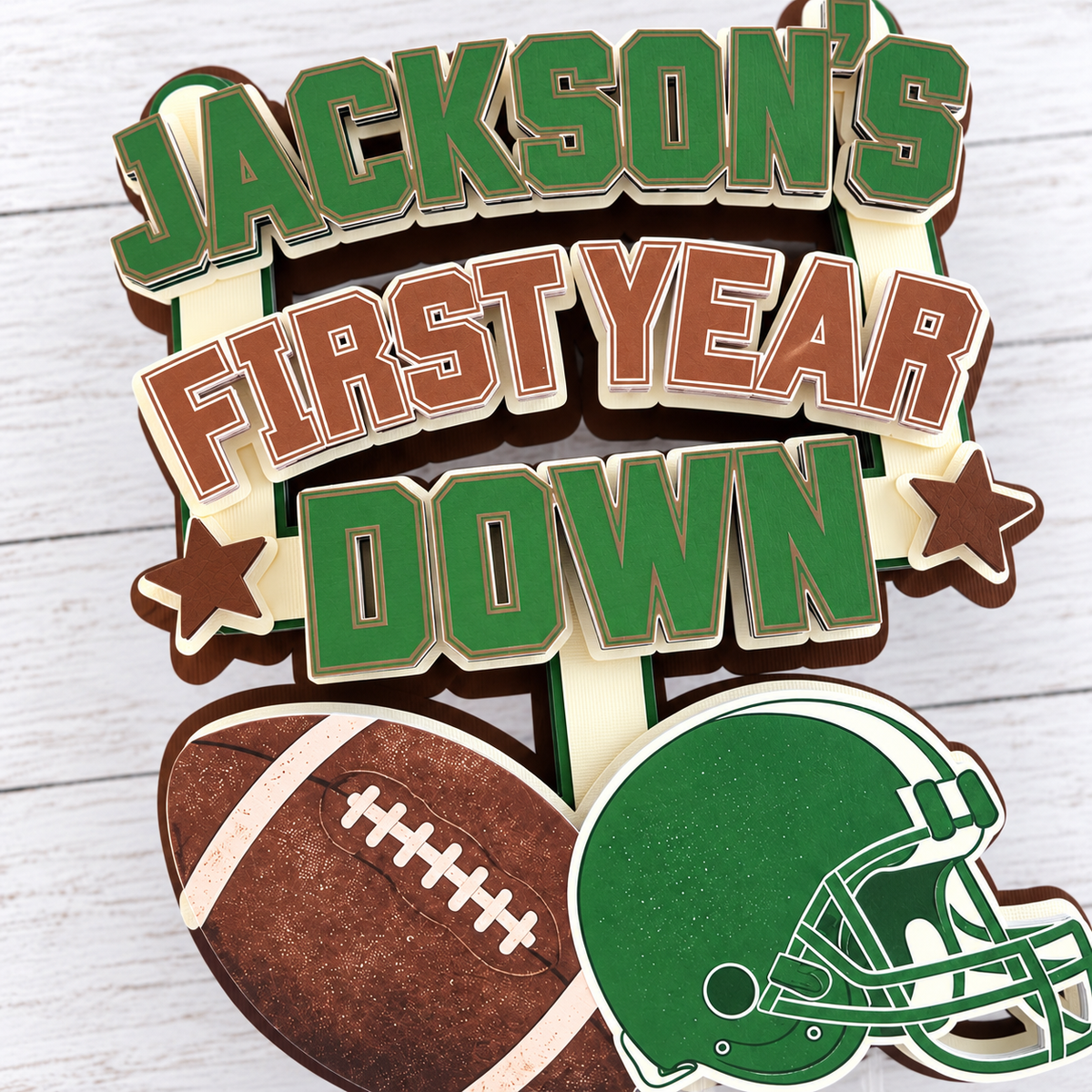 Detailed close up of layered cardstock First Year Down football cake topper showing dimensional lettering football helmet and handcrafted construction