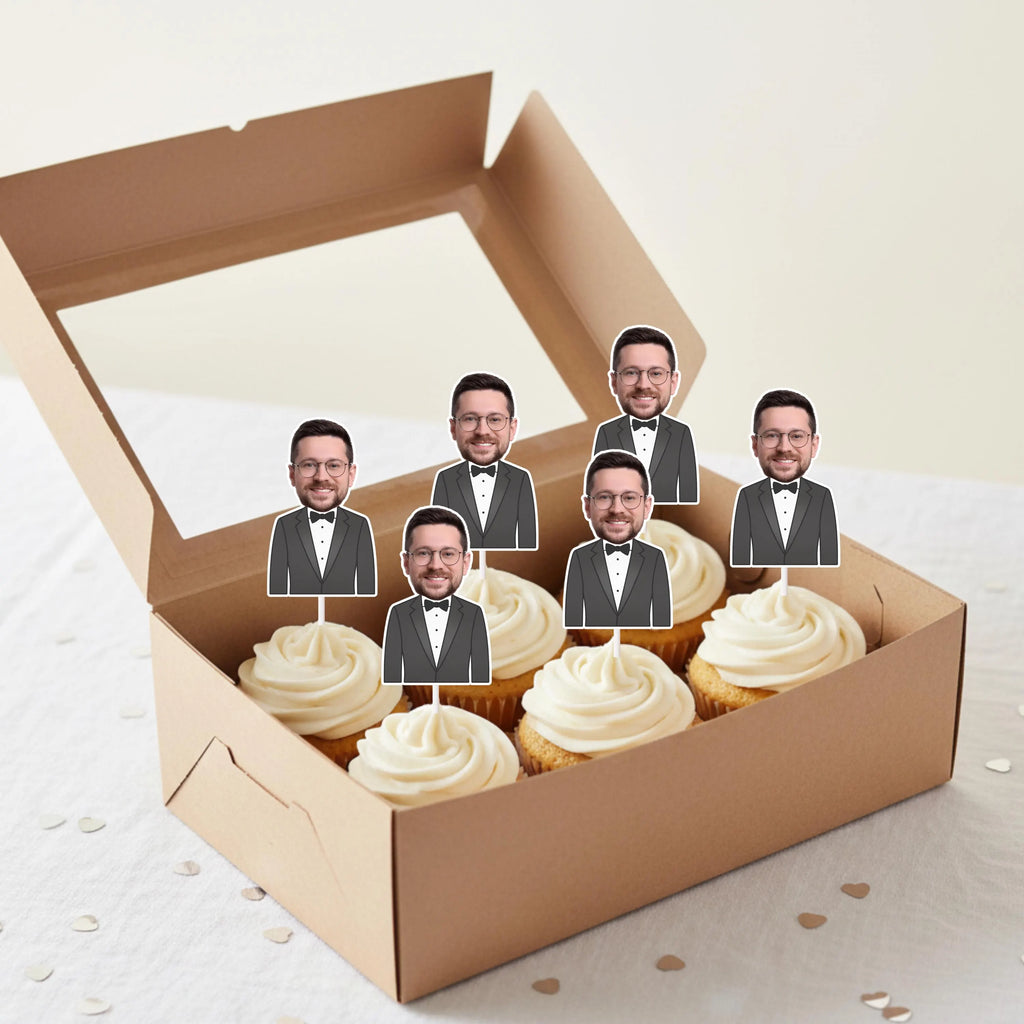 Box of Groom cupcakes with face cutouts of a man in a suit on top. 
