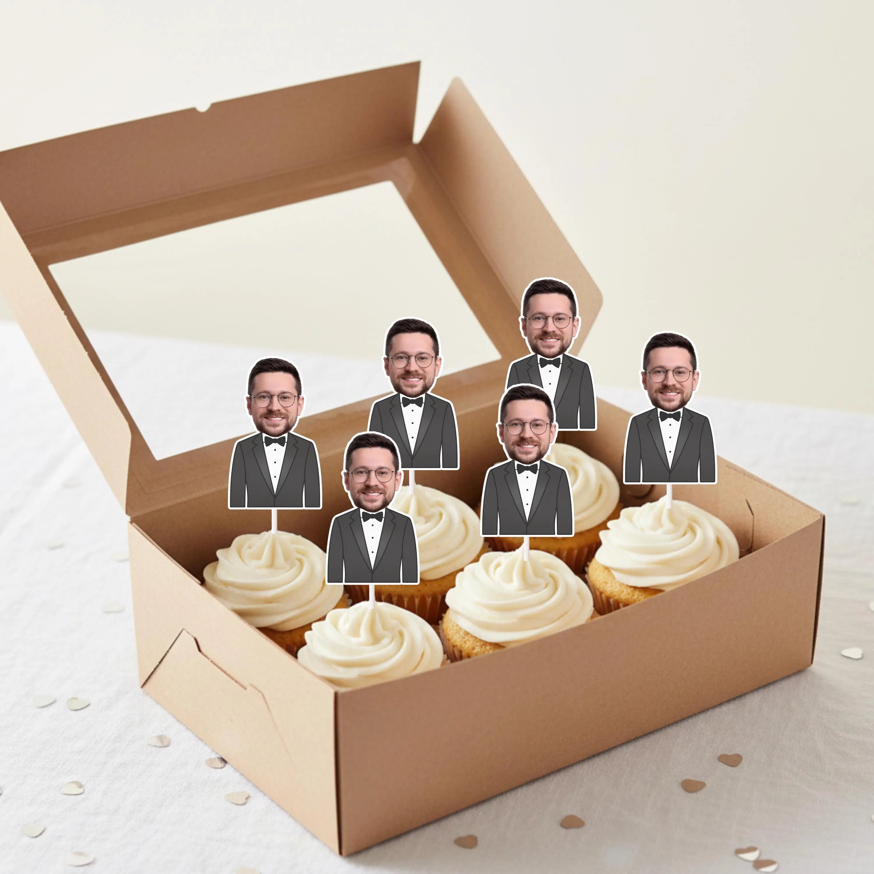 Box of Groom cupcakes with face cutouts of a man in a suit on top. 