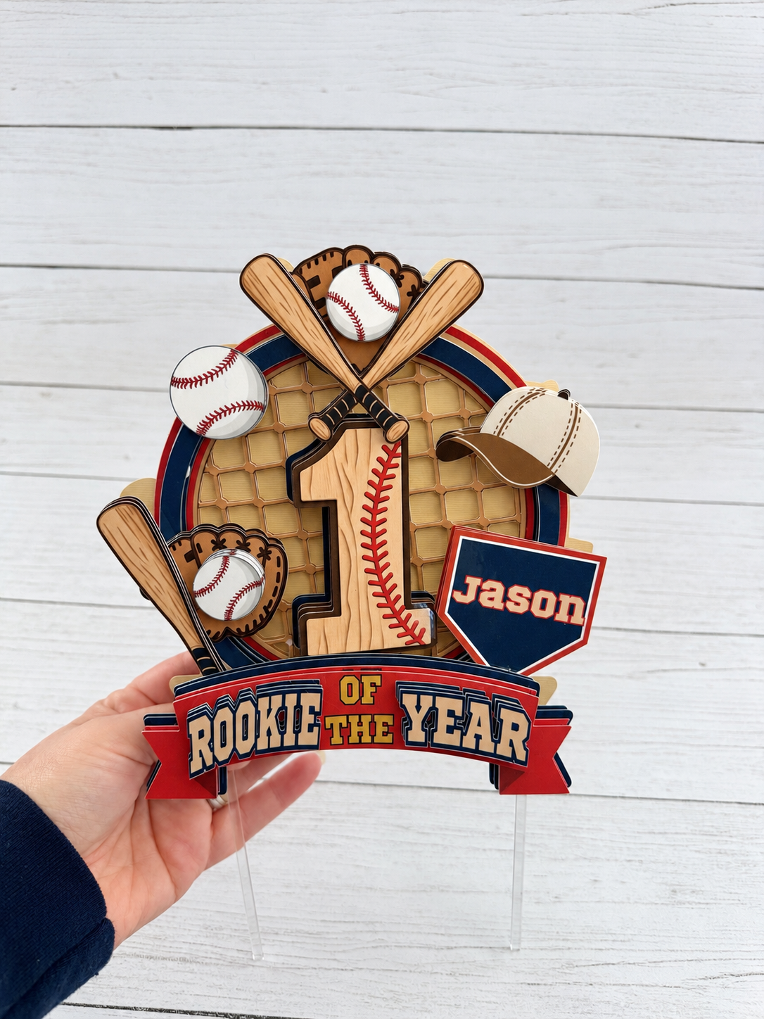 Hand holding personalized Rookie of the Year baseball cake topper showing standard size, clear cake sticks and layered cardstock construction