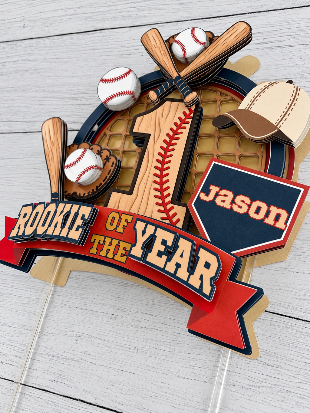 Close up angled view of layered Rookie of the Year baseball cake topper showing 3D cardstock details, bats, baseballs, glove, cap and personalized name