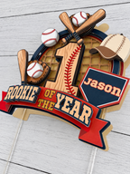 Close up angled view of layered Rookie of the Year baseball cake topper showing 3D cardstock details, bats, baseballs, glove, cap and personalized name