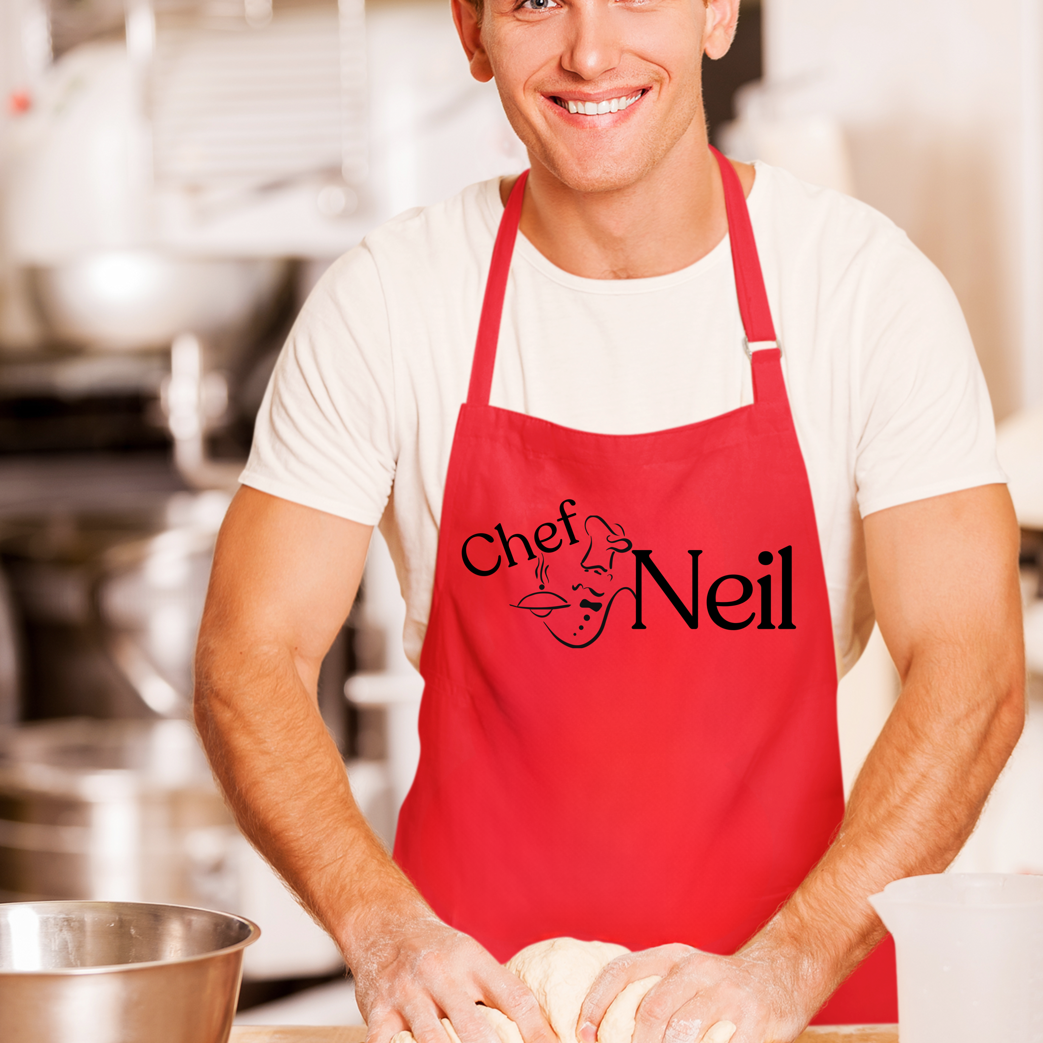 Man wearing a red apron with 'Chef Neil' printed on it, standing in a kitchen.