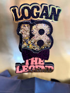 Decorative Gold and Black birthday Cake Topper with 'LOGAN 18 THE LEGEND' text on a blurred background
