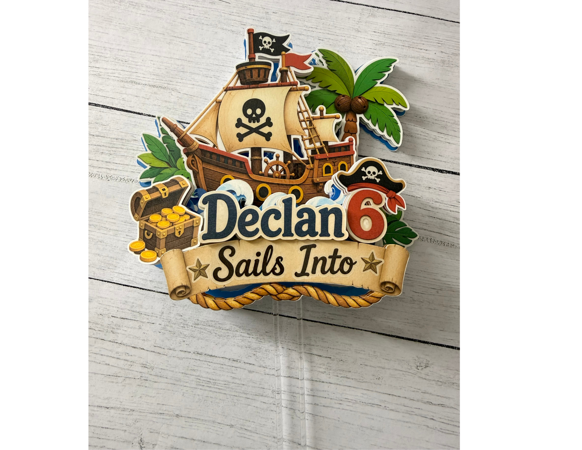 Full view of personalized pirate birthday cake topper with layered pirate ship treasure chest palm tree custom name age and clear cake picks.