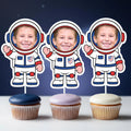 Three cupcakes with astronaut toppers on a dark blue background