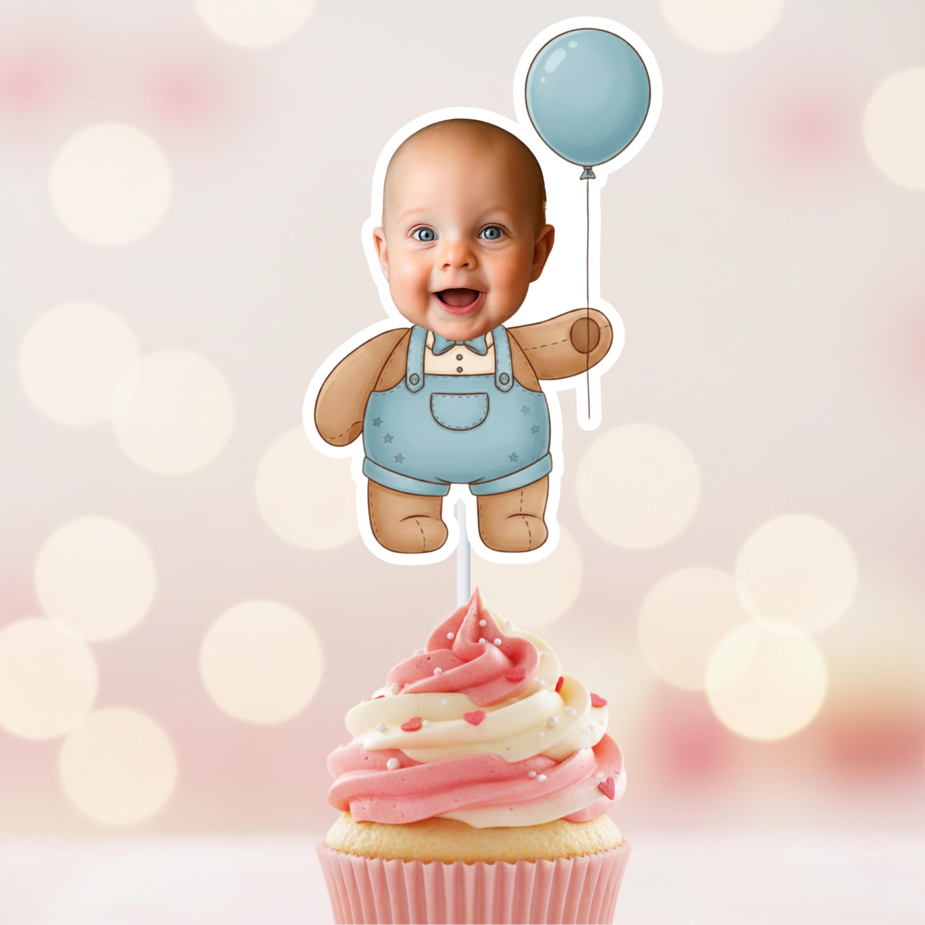 Baby-themed cupcake topper with a baby in overalls and a balloon on a pink and white cupcake against a blurred light background.