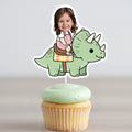 Cupcake with a dinosaur topper featuring a child's photo on a plain background