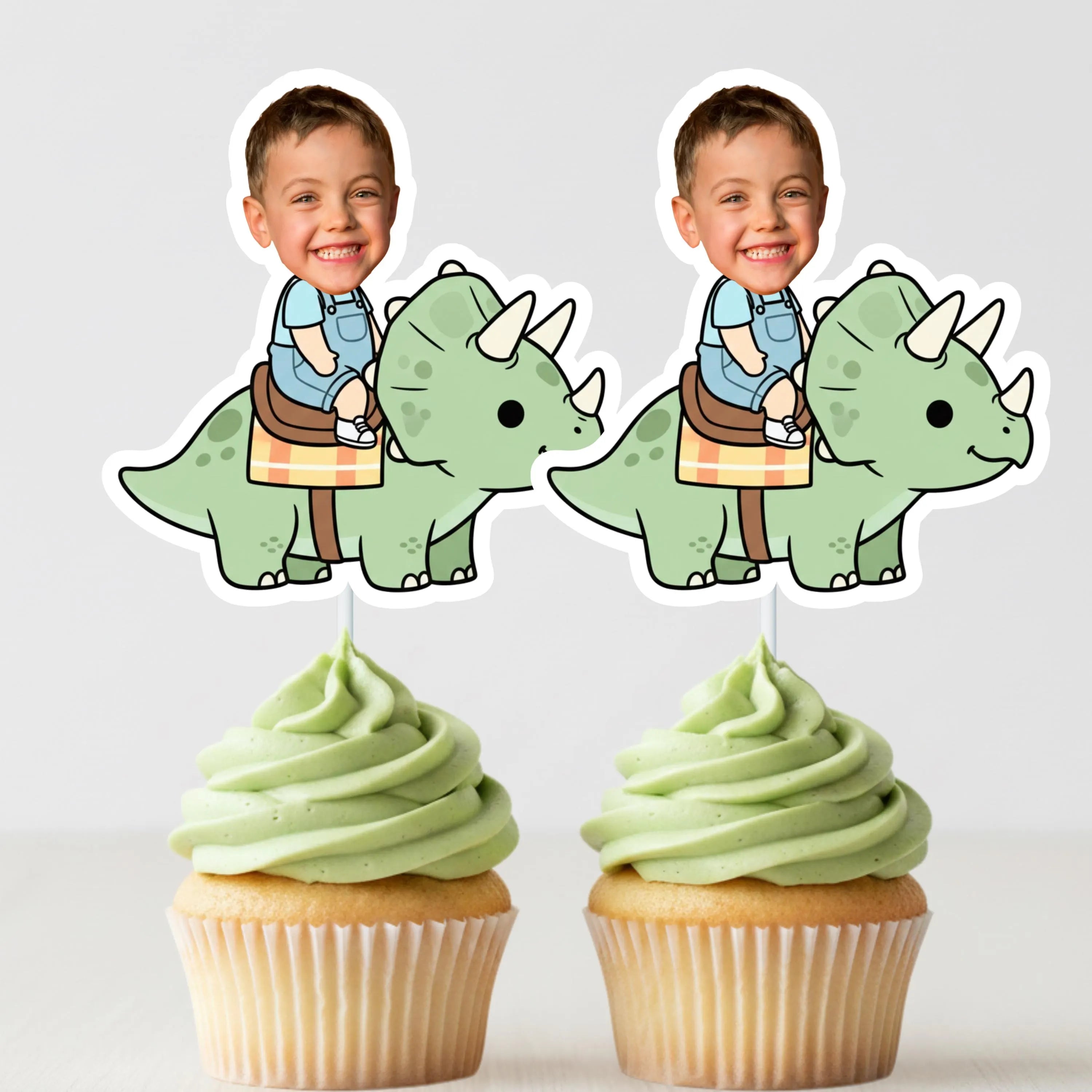 Two cupcakes with green frosting and dinosaur toppers on a white background