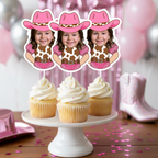 Personalized pink cowgirl cupcake toppers featuring a smiling toddler photo styled with a pink cowboy hat and western cow print outfit, displayed on vanilla cupcakes with white frosting. These custom western photo cupcake picks are perfect for a “My First Rodeo” birthday, pink cowgirl themed party, country western girl birthday celebration, barnyard birthday décor, and rustic rodeo dessert table styling. Designed for baby girl milestone birthdays, western themed smash cake sessions, and cowgirl party suppli