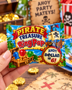 Personalized pirate Ring Pop party favor held by hand with treasure chest gold coins and pirate party decor in the background