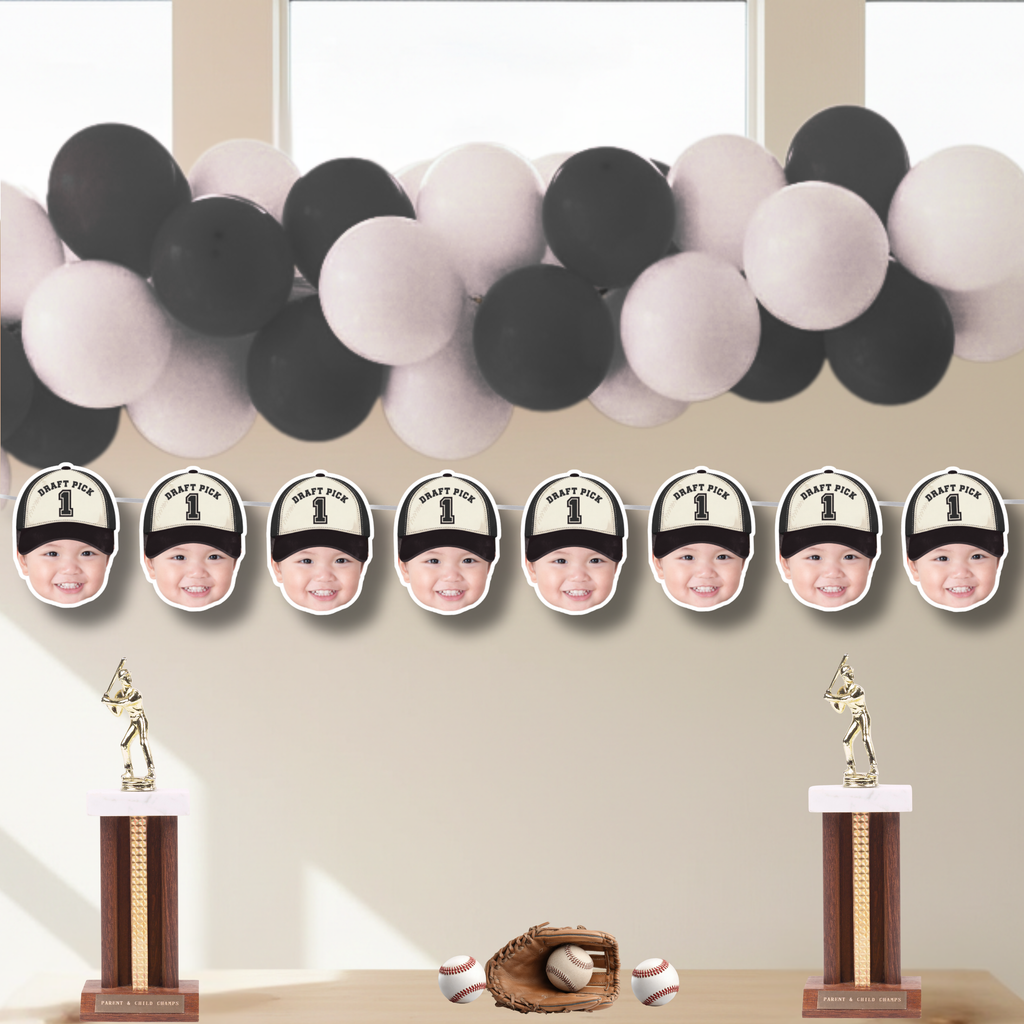 Rookie of the Year photo baseball banner with personalized Draft Pick 1 baby faces displayed under black and white balloon garland, styled as a modern sports birthday backdrop for baseball cake smash and little slugger celebration.
