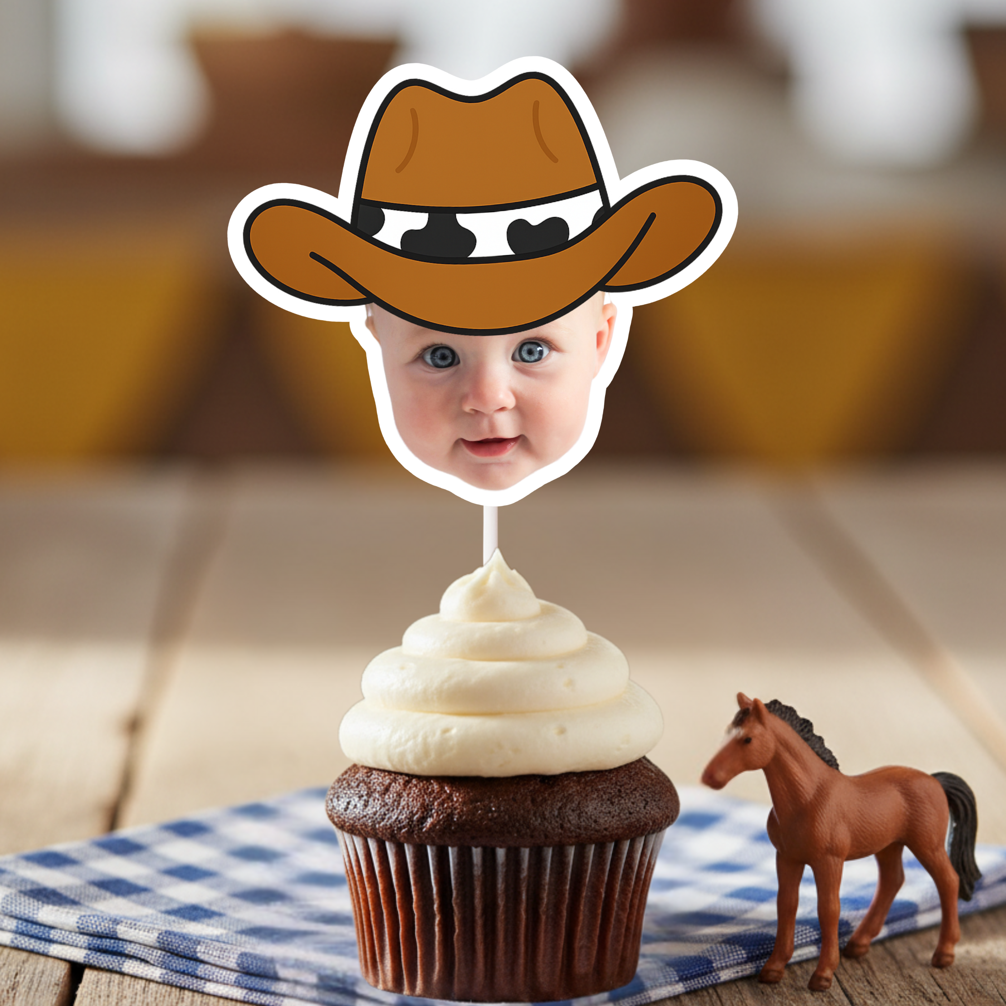 Close up of personalized cowboy baby face cupcake topper on chocolate cupcake with white frosting, styled with blue gingham napkin and toy horse accent. Ideal for cowboy first birthday parties, country themed baby celebrations, and western dessert table décor. Custom baby photo cupcake decoration highlighting child’s face.