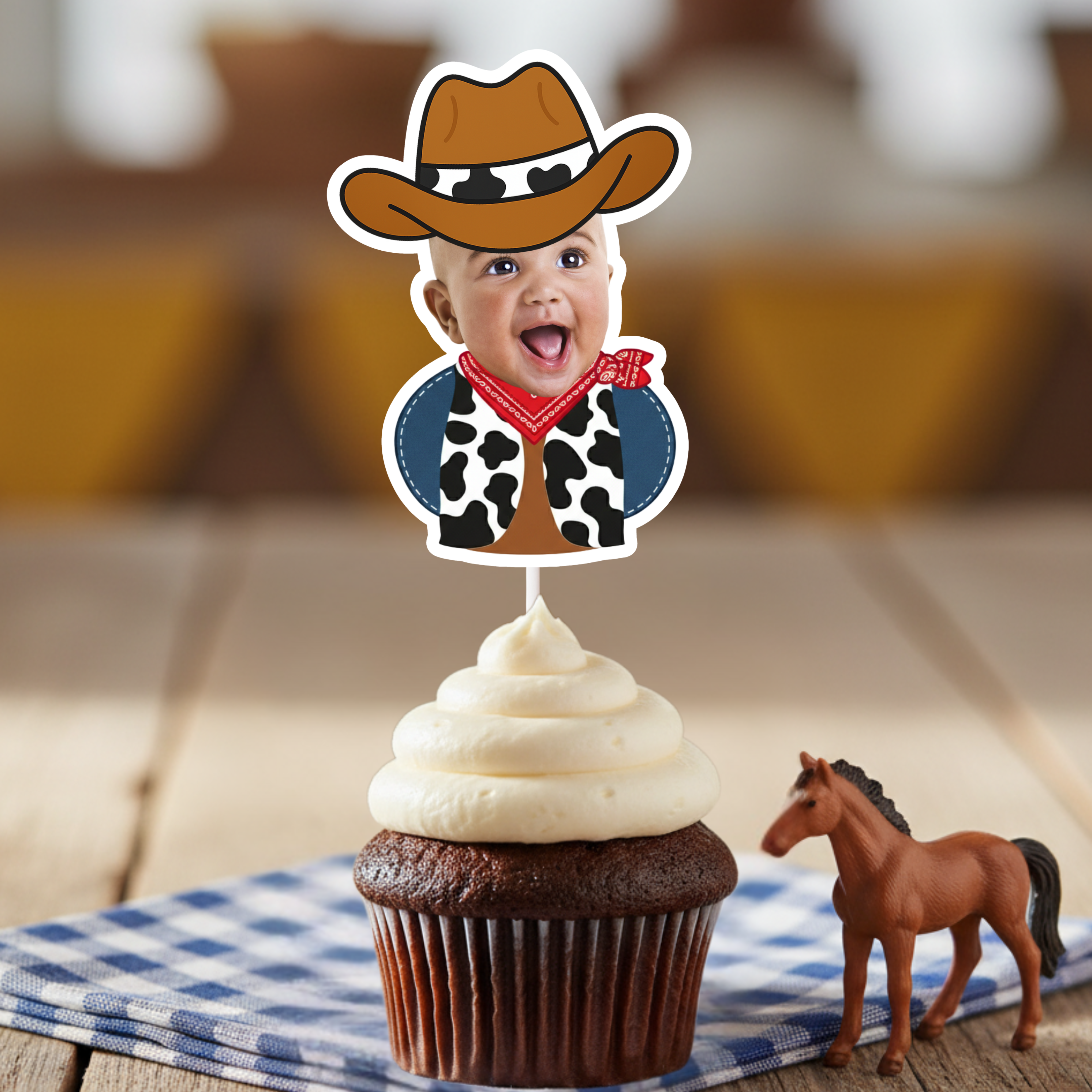 Single personalized cowboy baby photo cupcake topper displayed on chocolate cupcake with western toy horse and blue gingham napkin background. Ideal for cowboy first birthday parties, country themed baby celebrations, rodeo milestone events, and barnyard birthday décor. Custom face cupcake decoration designed to showcase the child’s photo for western party themes.