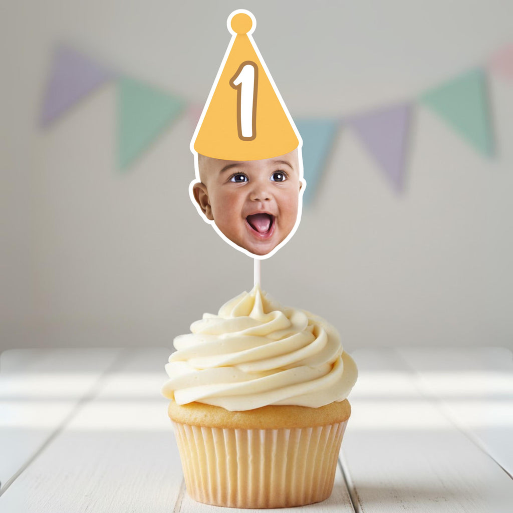 Cupcake with a photo of a baby on top, wearing a party hat with the number 1, against a light background with colorful flags.