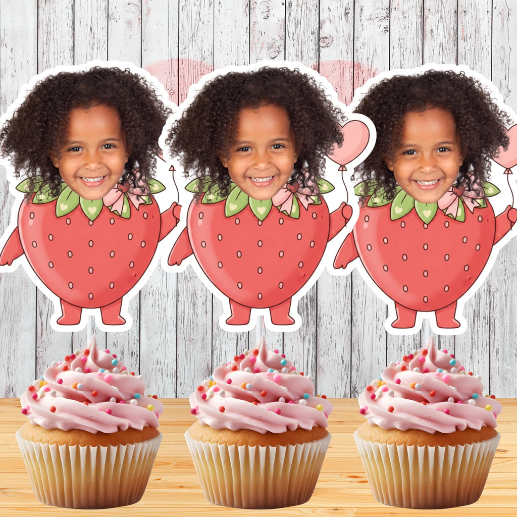 Three strawberry-shaped cutouts with a child's face on top, placed above cupcakes with pink frosting and sprinkles.