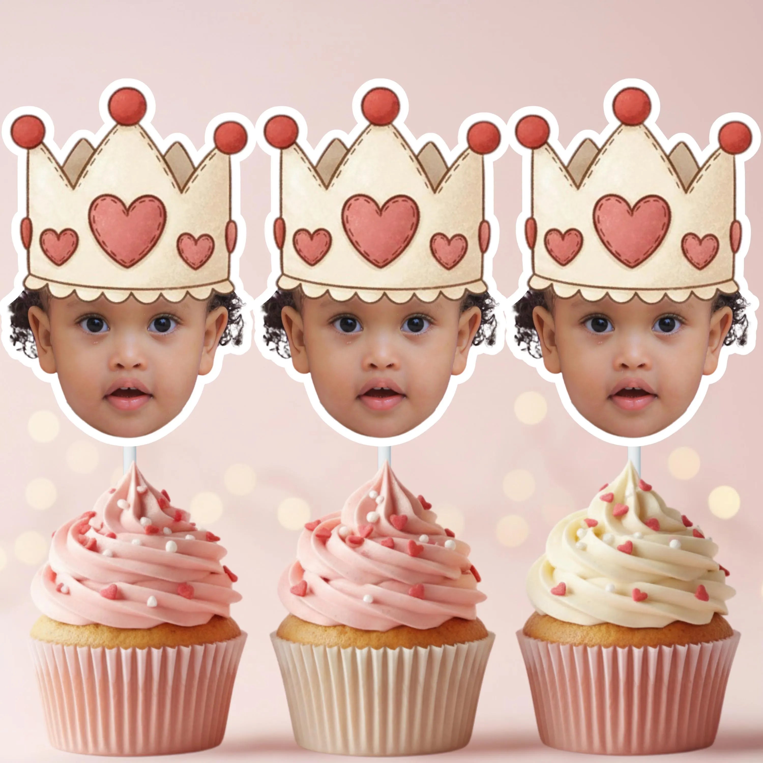 Three cupcakes with pink frosting and heart decorations, each topped with a cardboard crown featuring hearts.