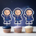 Three cupcakes with astronaut-themed toppers against a dark blue background