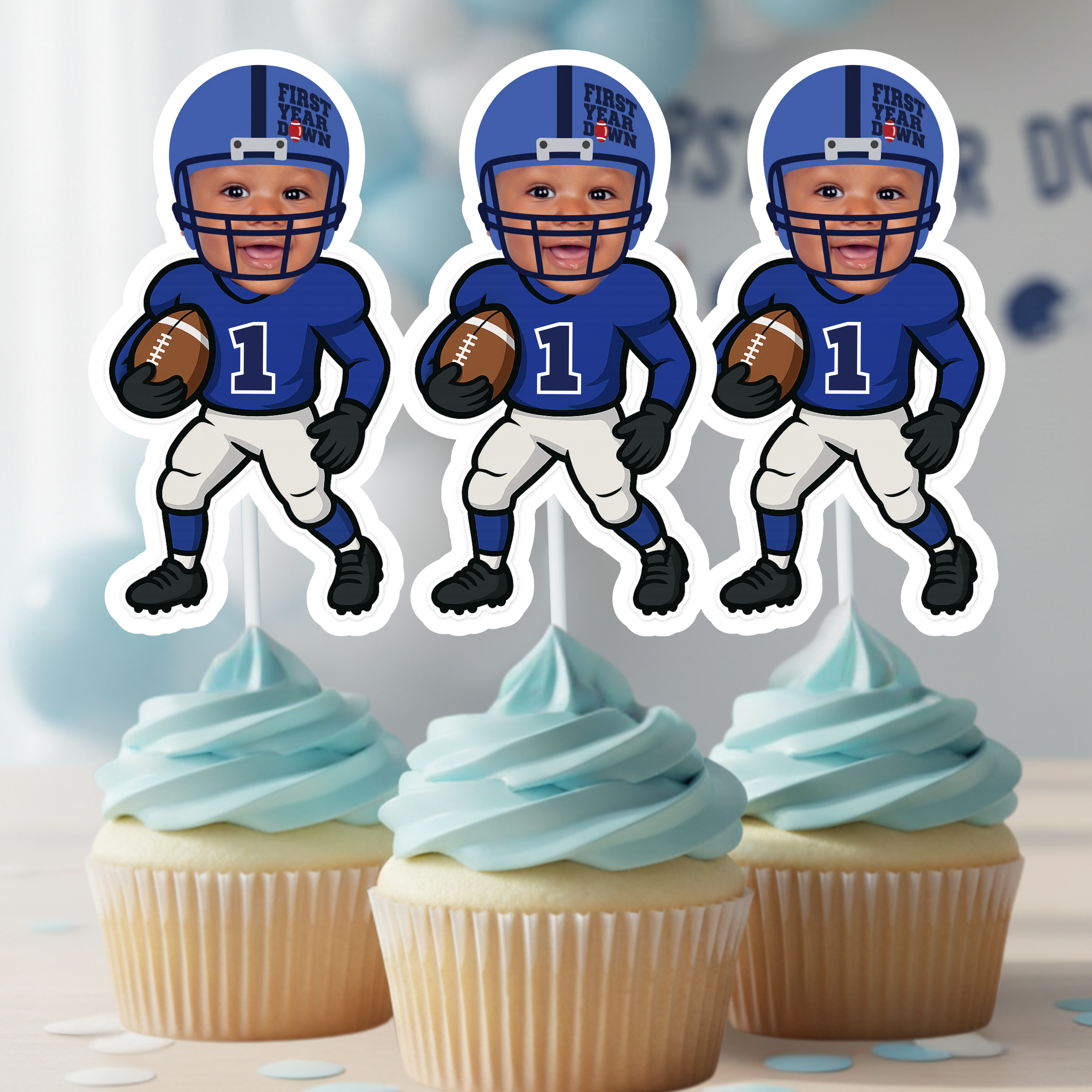 Three personalized First Year Down football cupcake toppers featuring a custom baby photo are displayed on blue frosted cupcakes. This first birthday sports party decoration is perfect for a football-themed cake smash, dessert table setup, or baby boy milestone celebration. Ideal for a “One Year Down” birthday theme with coordinated blue and green balloon decor.