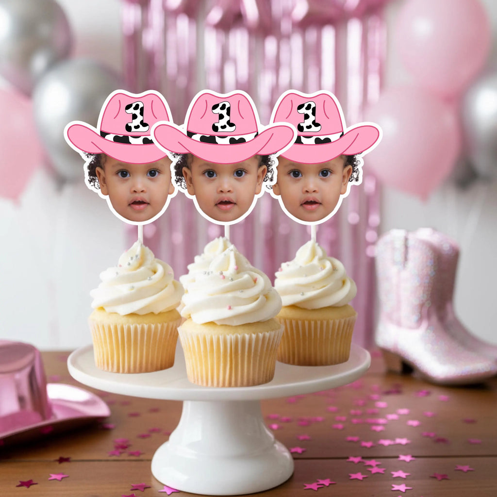 Three cupcakes with pink cowboy hats on a white cake stand against a pink and gray balloon background.