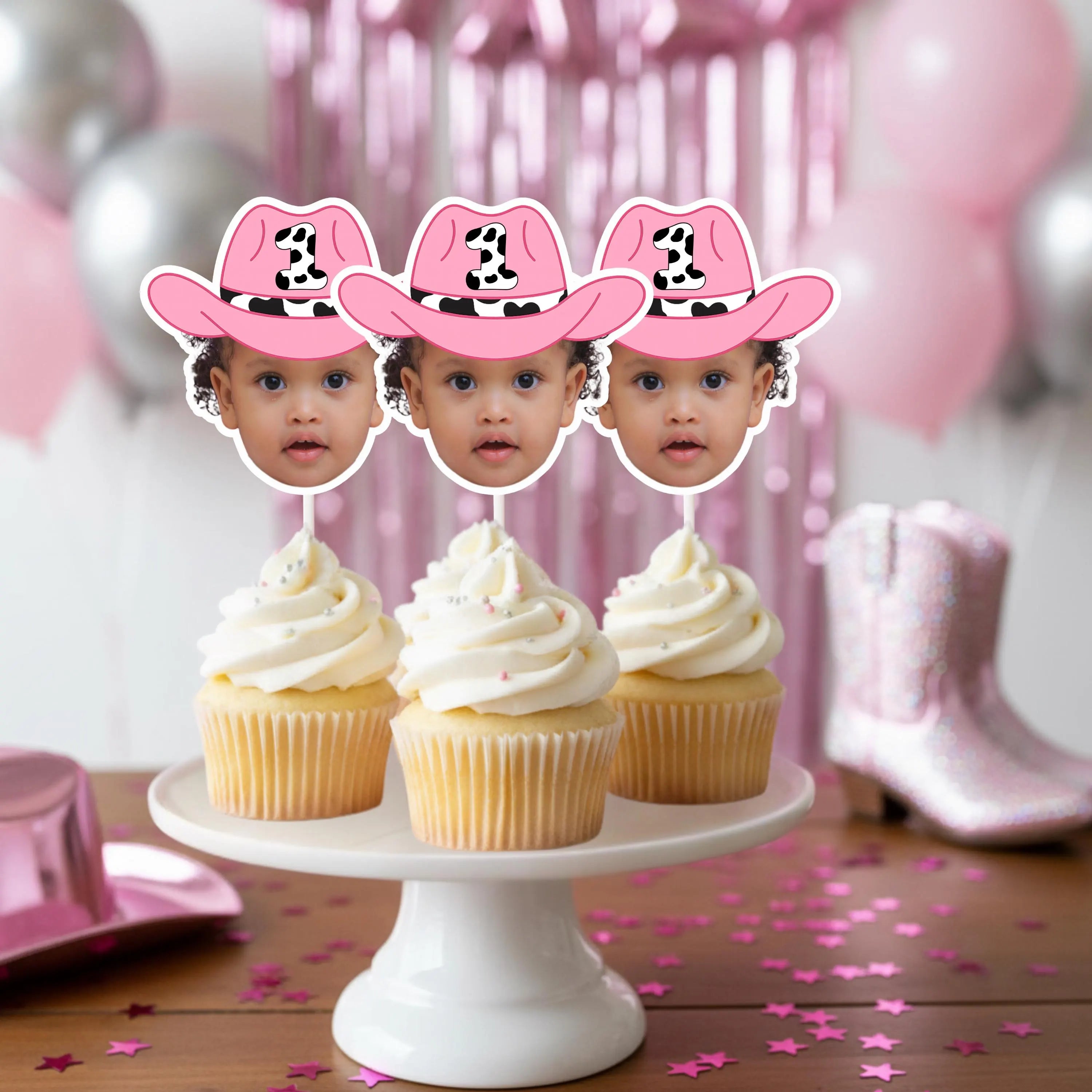 Three cupcakes with pink cowboy hats on a white cake stand against a pink and gray balloon background.