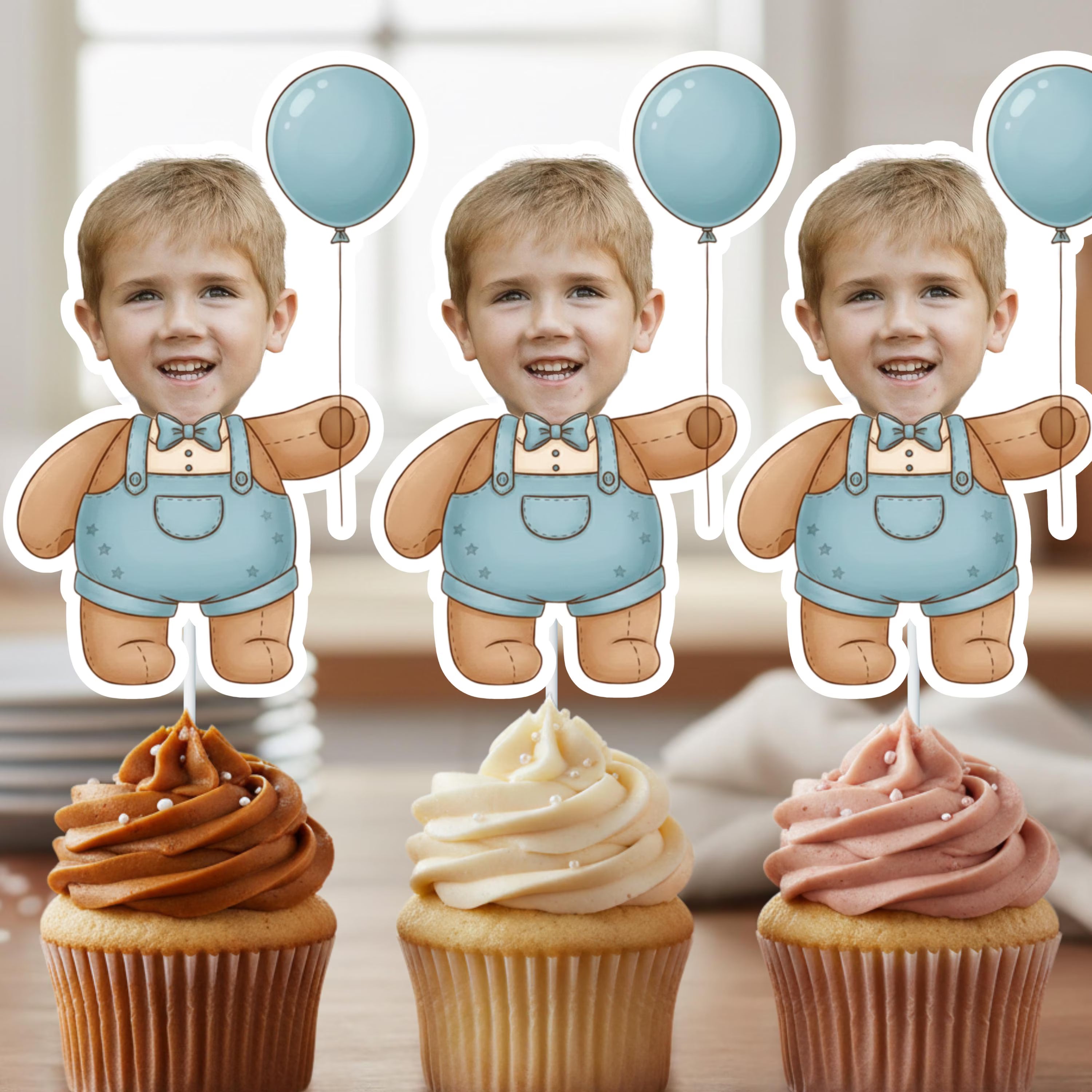 Three cupcakes with different colored frostings and a child's face cutout in overalls and balloons.