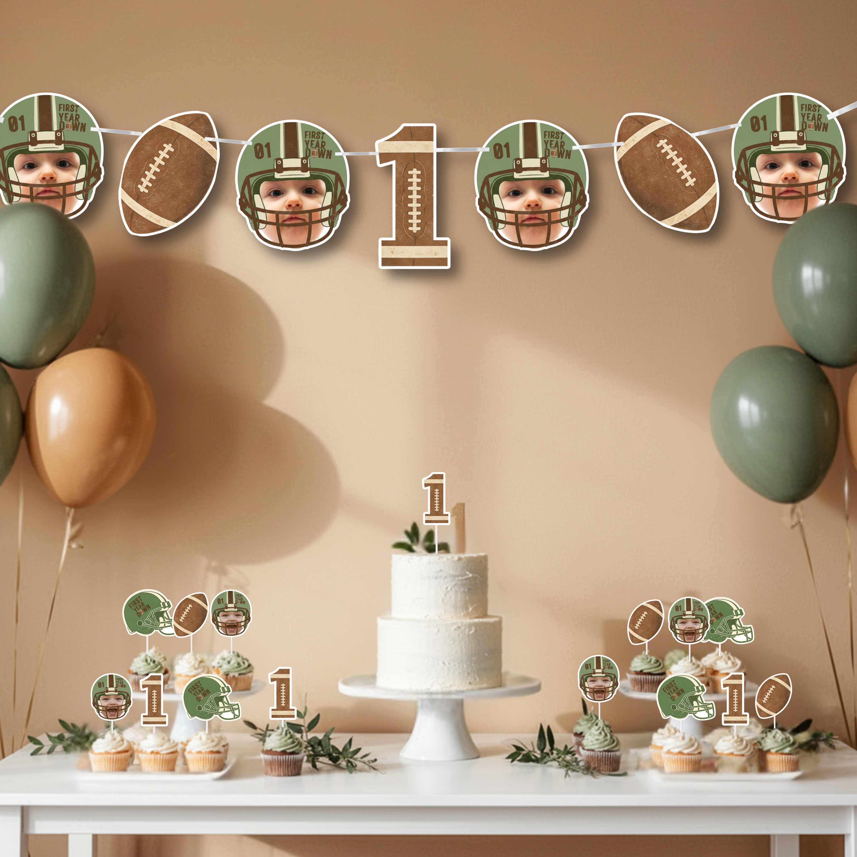 First Year Down football first birthday banner styled above a neutral dessert table with smash cake, cupcakes, and sage green and tan balloons. Custom photo football banner decor designed for a sports themed one year old birthday party celebration.