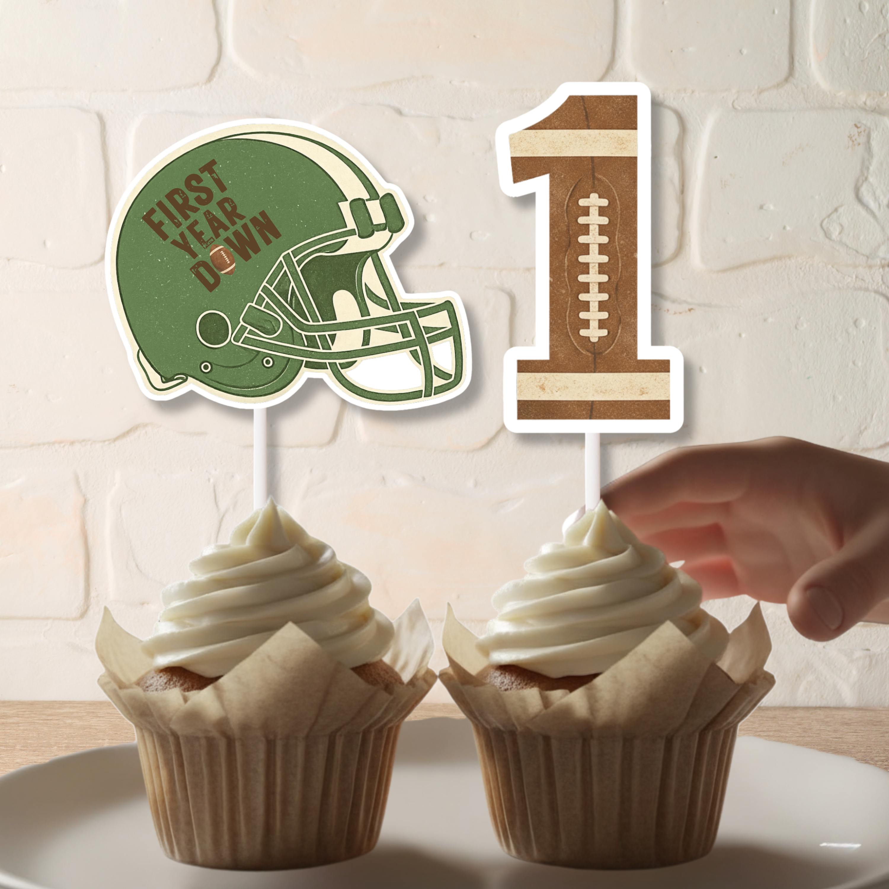 Close up of First Year Down football helmet cupcake topper and textured number one topper placed in vanilla cupcakes. This personalized football first birthday decoration adds a sporty touch to a Rookie of the Year dessert table setup.