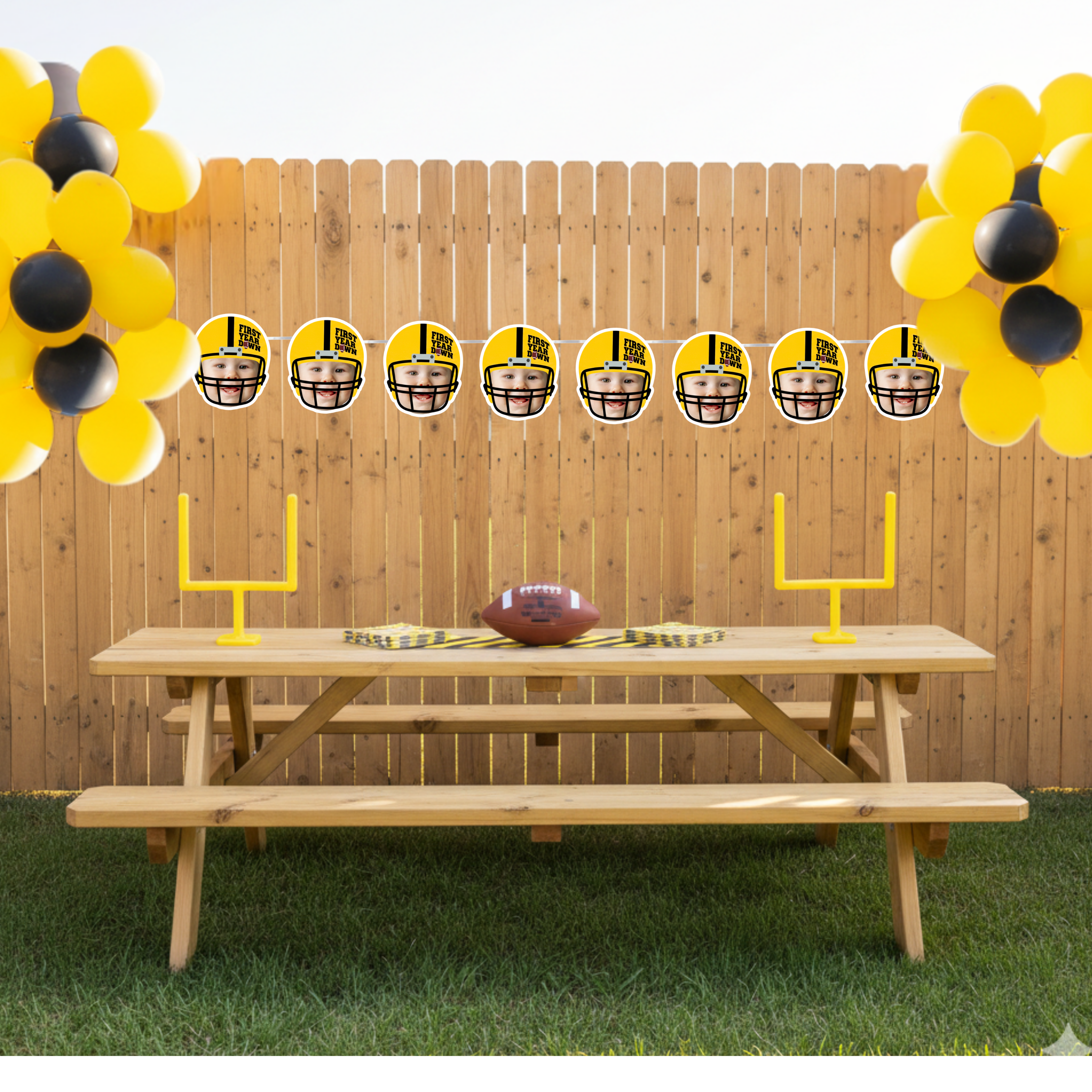 Football first birthday photo banner hanging across a backyard tailgate themed party with yellow and black balloons and mini goal posts. Personalized First Year Down helmet banner with baby face photos styled for an outdoor game day birthday celebration.