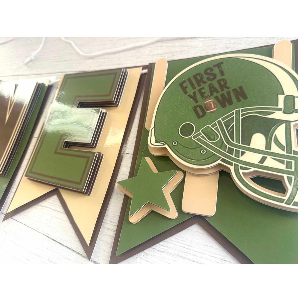 Closeup of layered sage green football helmet and star detail on the First Year Down highchair banner