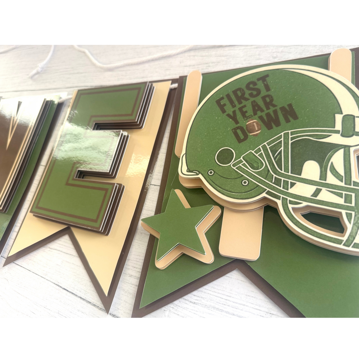 Closeup of layered sage green football helmet and star detail on the First Year Down highchair banner