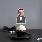 Cupcake with a topper of a man in a suit on a dark surface with a gray background
