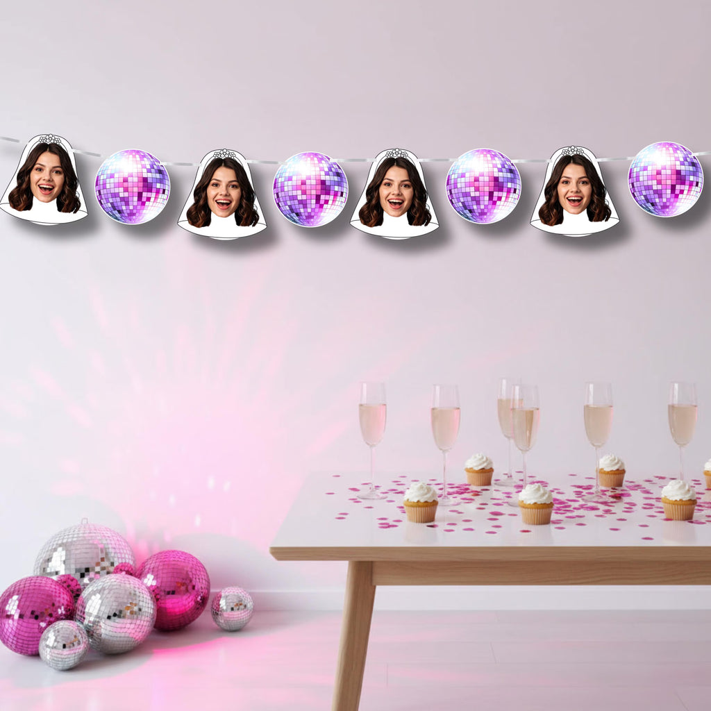 Decorative string with face cutouts and disco balls above a table with drinks and cupcakes.