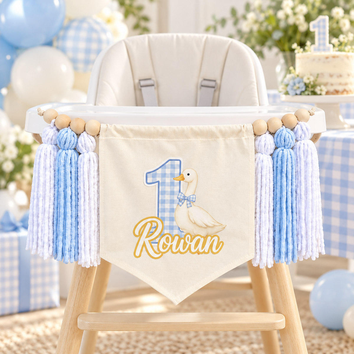 Baby blue One Silly Goose personalized first birthday high chair banner displayed on a white high chair with gingham party decor and a first birthday cake.